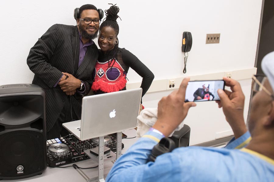 People smiling at DJ booth and having their photo taken.  Open Gallery